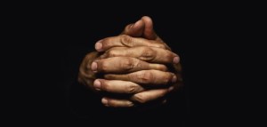 Male hands crossed for prayer in dark